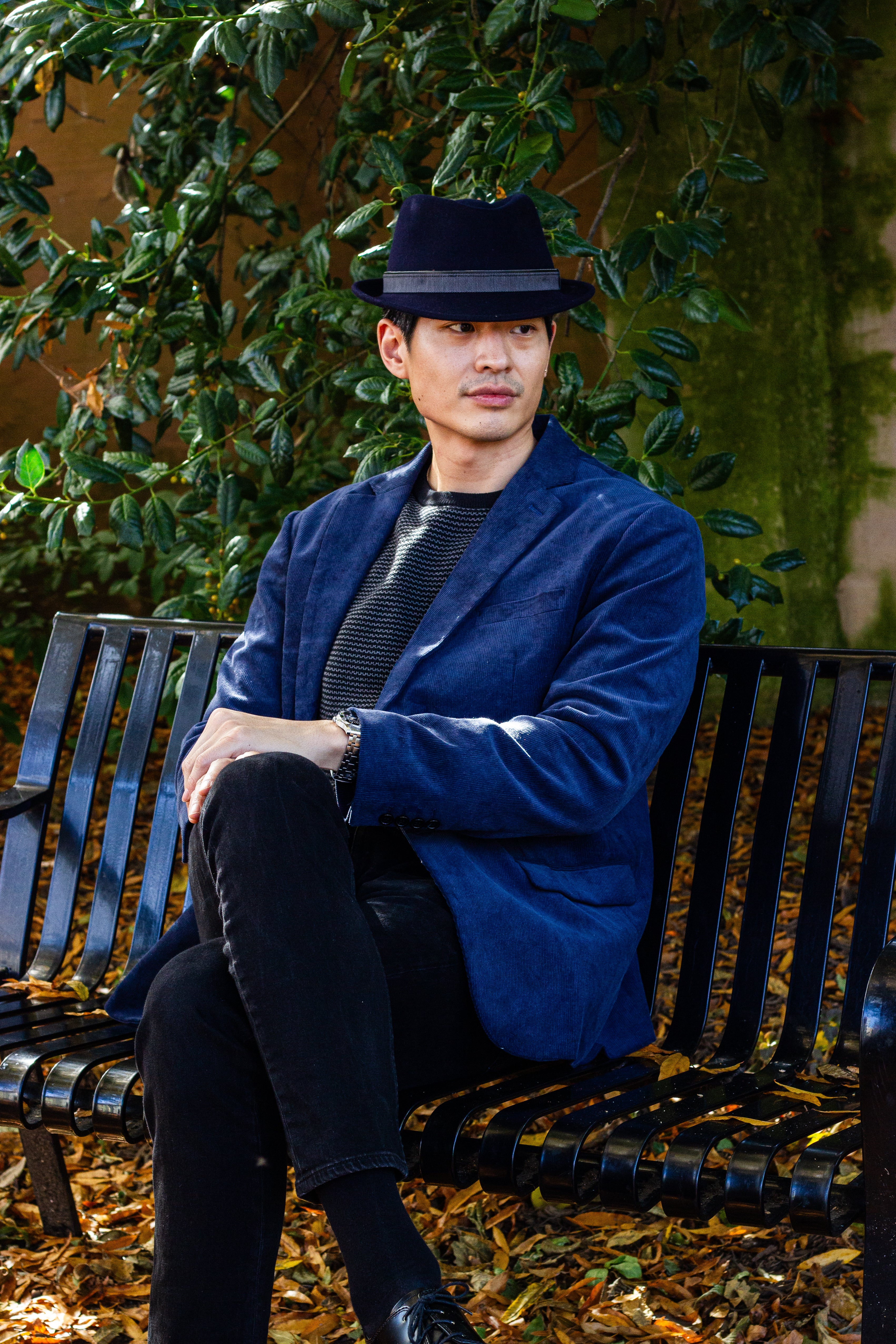 Man on bench in blue jacket & black fedora